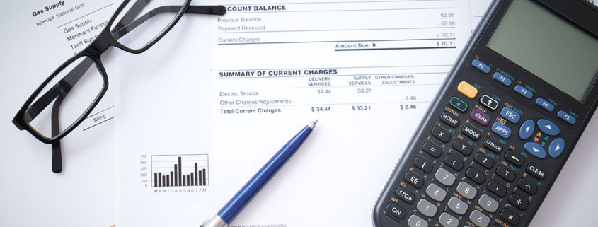 calculator, glasses and pen on top of electrical bill while potential plug load energy savings are being calculated