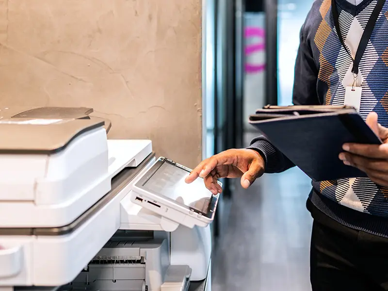 African American in his 30s wearing a pattern sweater using an office copier.